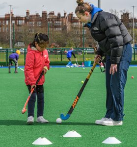 A coach helping a young player with her stick technique on the pitch