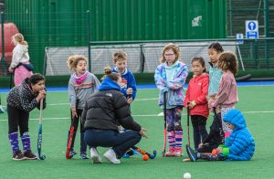 A coach crouching with a group of primary age players holding hockey sticks