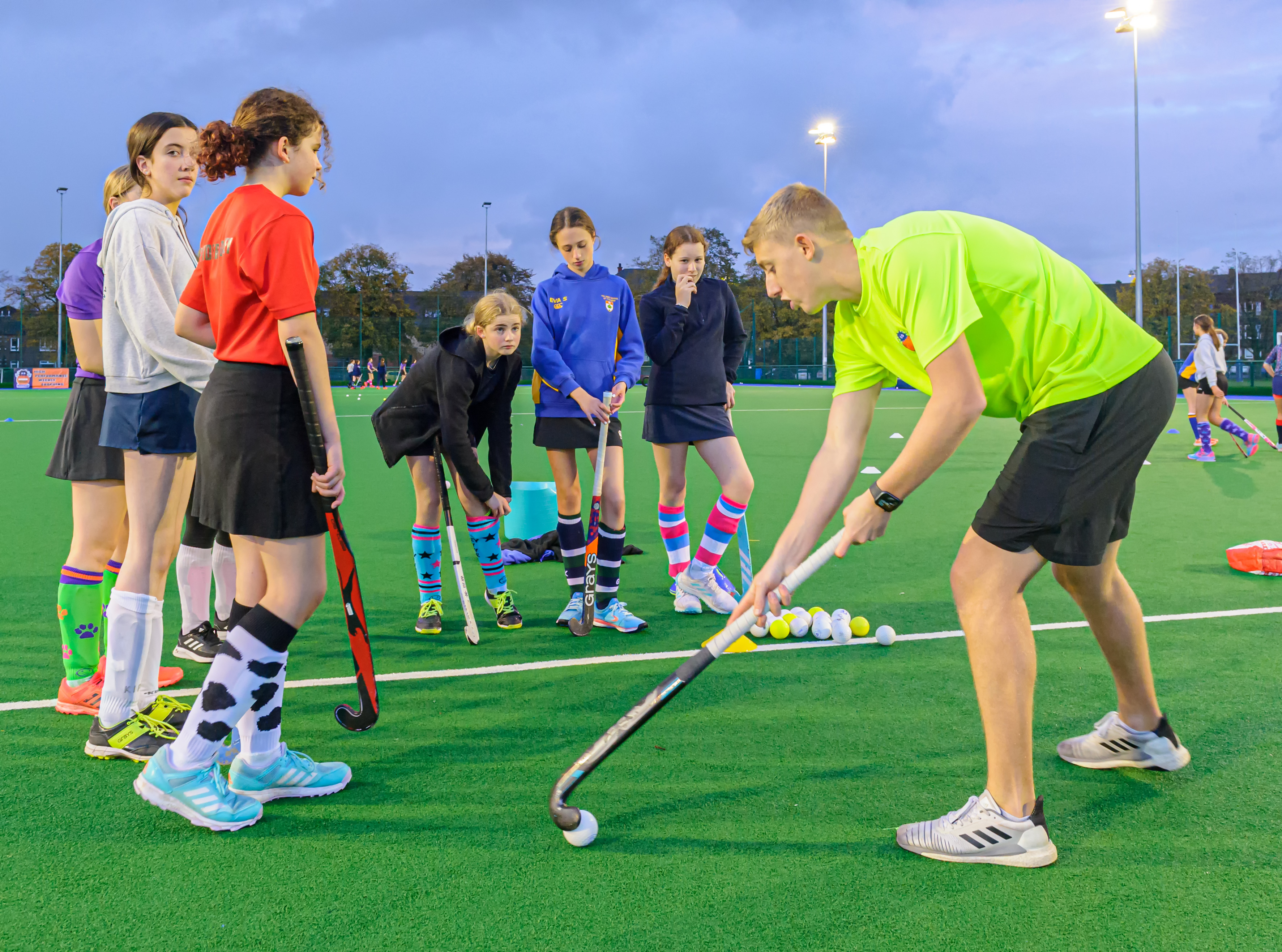 A Spider Hockey coach demonstrating a drill to a group of young players on an outdoor pitch