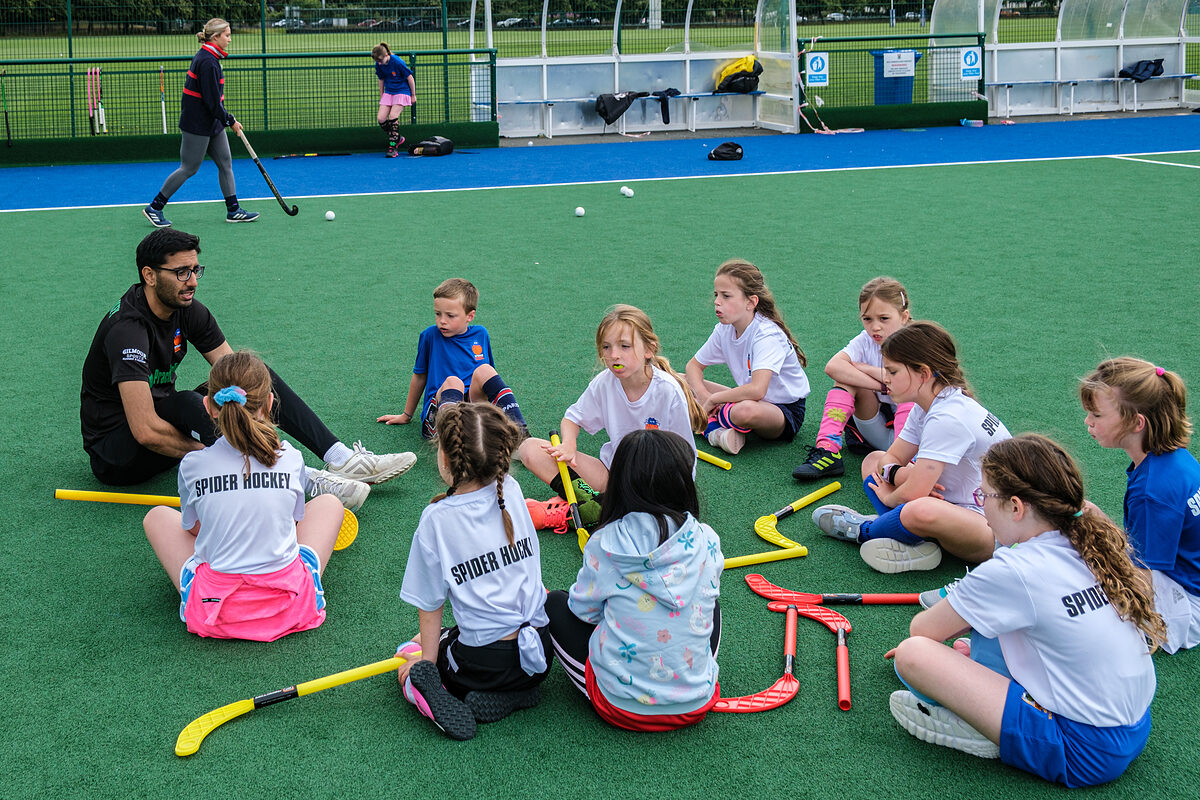 Players gathered in a huddle with their coach at a Spider Hockey camp